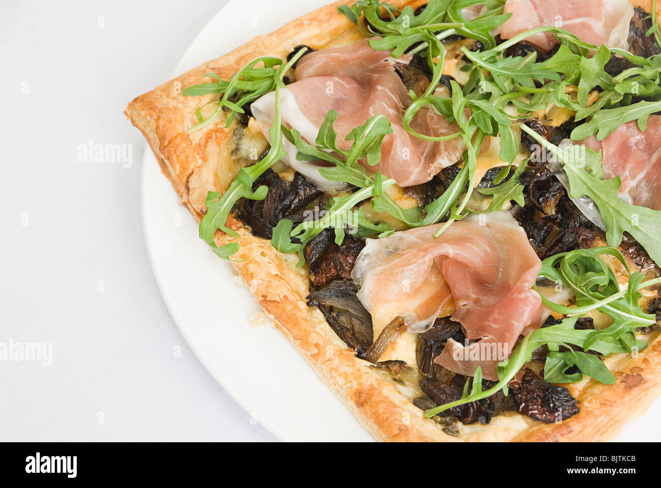 Filo pasta pizza guarnita con prosciutto, cipolle caramellate e rucola Foto Stock