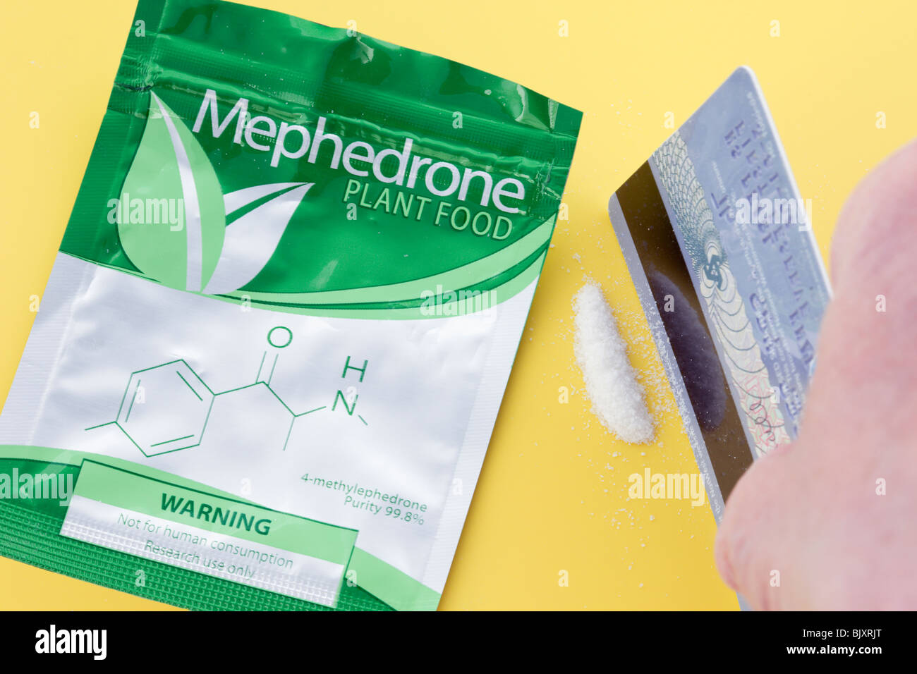 La Gran Bretagna, il Regno Unito, l'Europa. Persona che utilizza carta per effettuare una linea di Mephedrone farmaco per sbuffare con pacchetto di cibo vegetale. Foto Stock