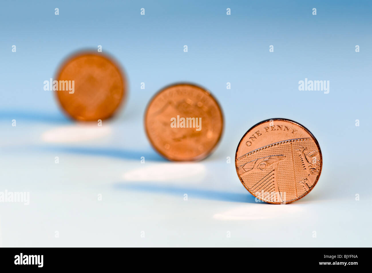 Tre un penny pezzi in linea diagonale contro uno sfondo blu con la seconda e la terza delle monete in euro al di fuori della messa a fuoco Foto Stock