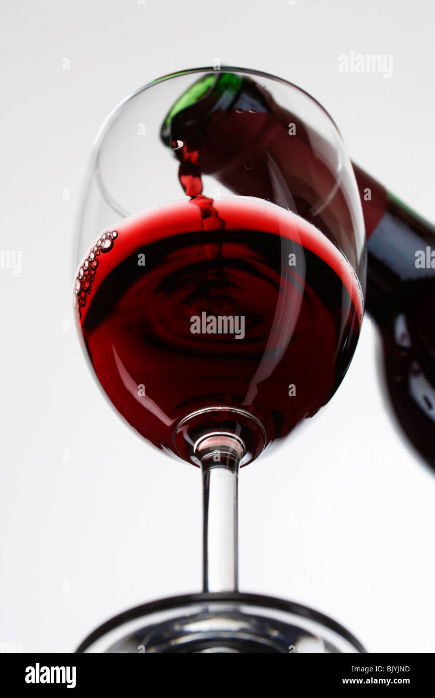 Vino rosso versare in un bicchiere su sfondo bianco Foto Stock