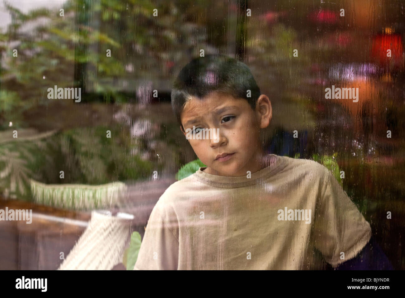 Multicultural multi-culturale di bambino 9 -10 anni vecchio ragazzo ispanico guardando fuori attraverso una finestra in un giorno di pioggia.riflessivo dreaming seduta signor © Myrleen Pearson Foto Stock