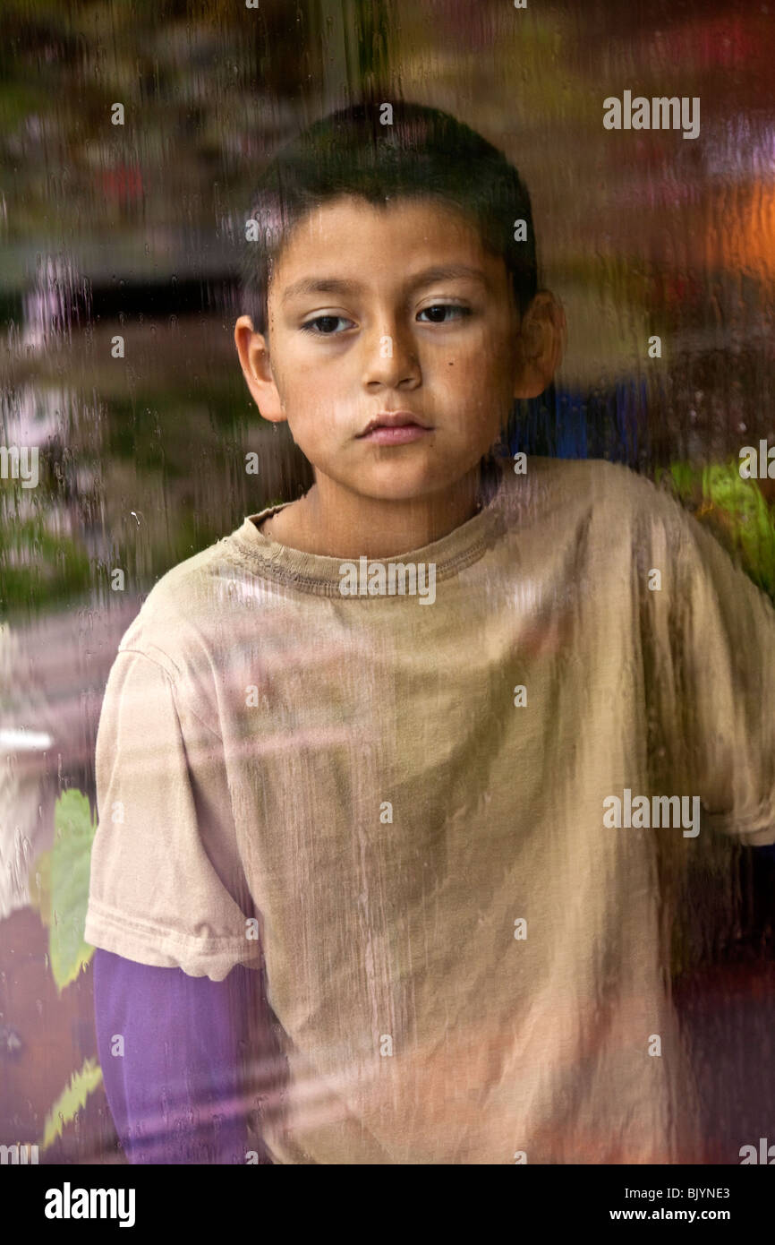 Multicultural multi-culturale di bambino 9 -10 anni vecchio ragazzo ispanico guardando fuori attraverso una finestra in un giorno di pioggia. Signor © Myrleen Pearson Foto Stock