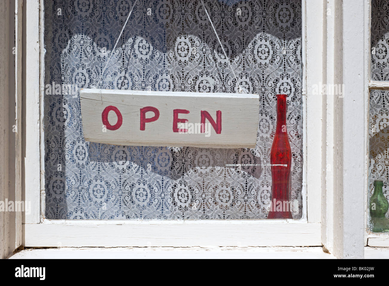 Un vecchio bianca con finestra con un segno aperto pendenti davanti tende di pizzo a Lincoln, Nuovo Messico. Foto Stock