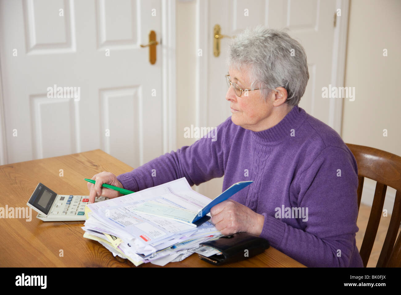 Senior indipendenti di donna titolare di pensione o di rendita con grande pila di banconote sul tavolo utilizzando una calcolatrice prima di scrivere controllare per pagare una bolletta NEL REGNO UNITO Foto Stock