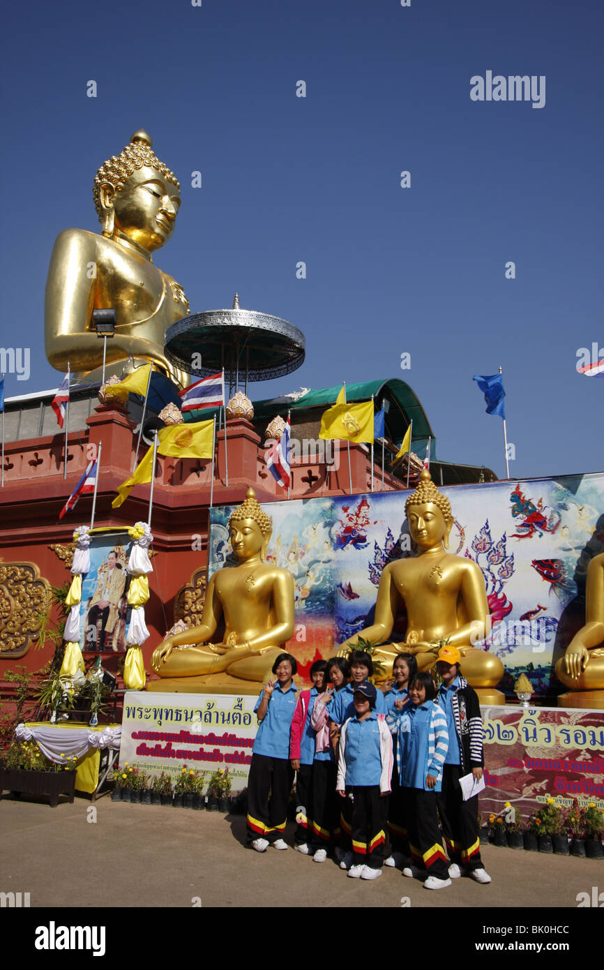 La scuola dei bambini pongono di fronte a un gigante Buddha d'oro a Sop Ruak, Il Triangolo d'oro, dal Mekong nella Tailandia del Nord Foto Stock