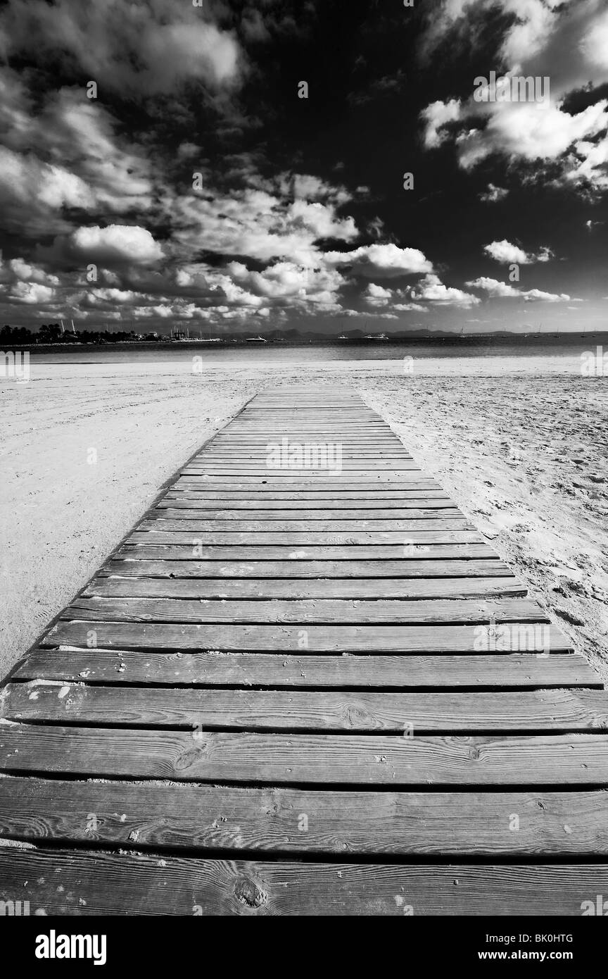 Drammatica vista di una passerella in legno che si estende lungo una spiaggia verso il mare a Alcudia, Spagna. Foto Stock