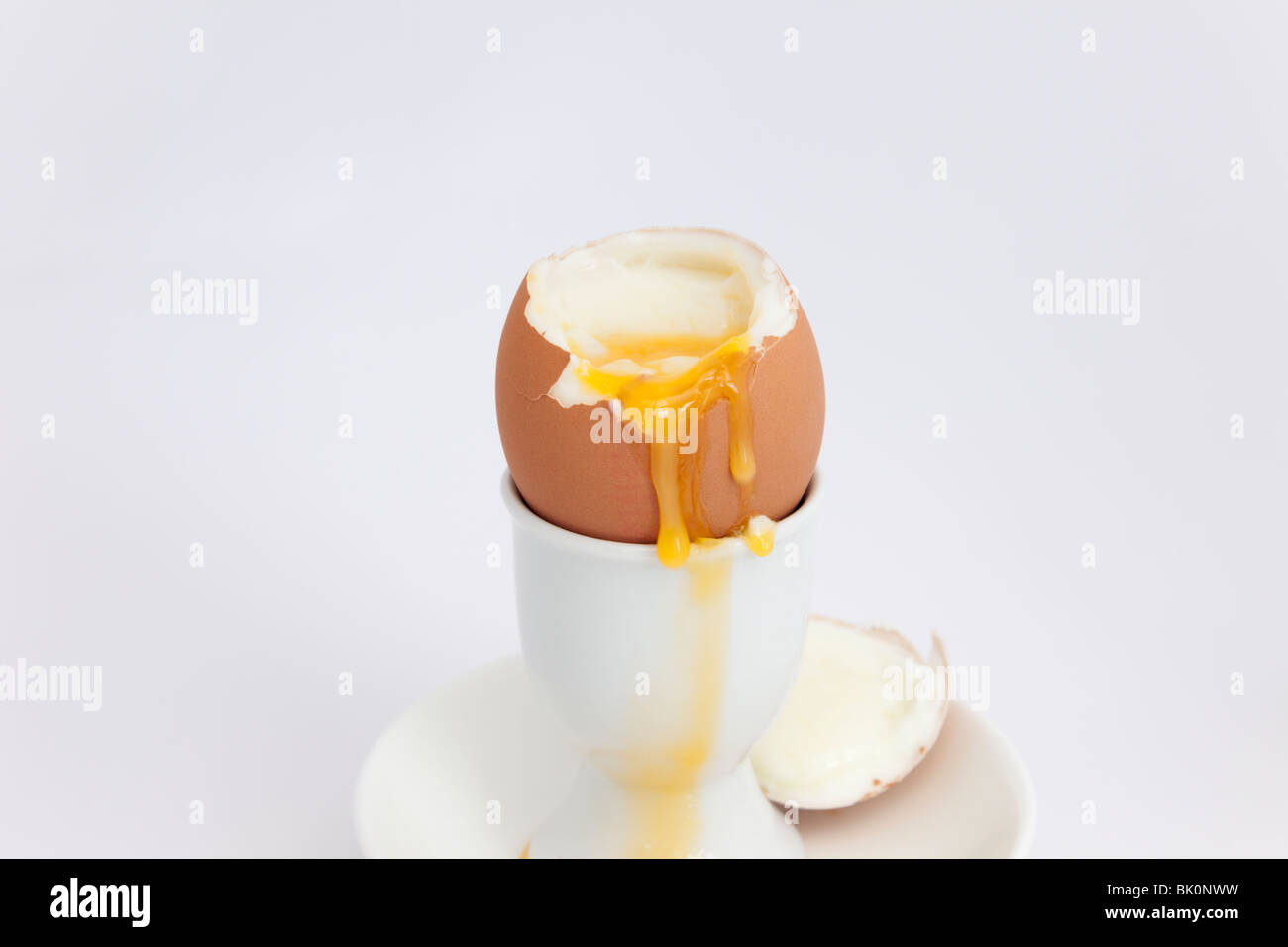 Un open uova sode con tuorlo che cola in un uovo cup su sfondo bianco Foto Stock
