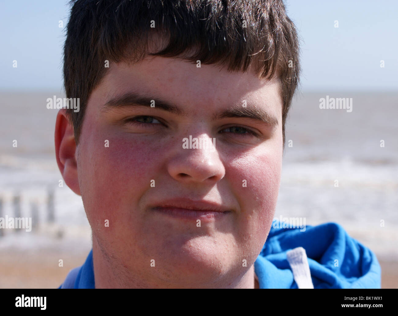 Fanciullo con il mare e la spiaggia dietro di lui. Egli è di 17 anni. Foto Stock