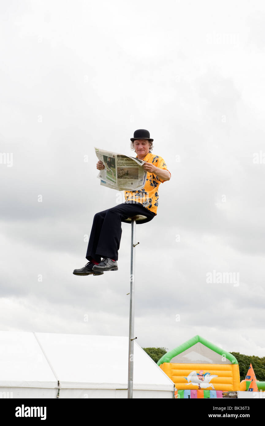 Uomo in cappello bowler seduti sulla cima di molto alte pole leggendo un giornale Foto Stock