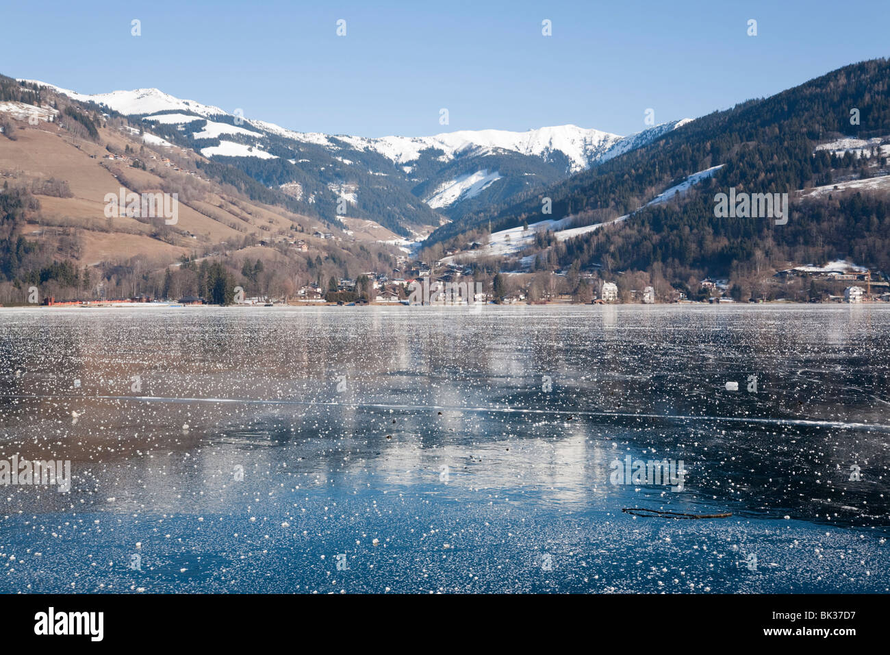 Congelati lago Zeller See con montagne innevate si riflette nel ghiaccio in località alpina. Zell am See, Austria, Europa Foto Stock