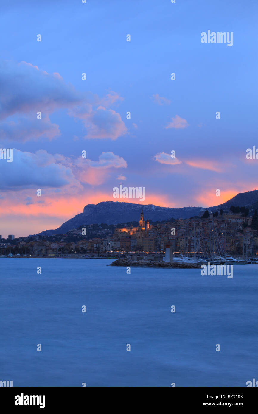 Nuvoloso Tramonto sulla costa e sulla città illuminata di Menton Foto Stock