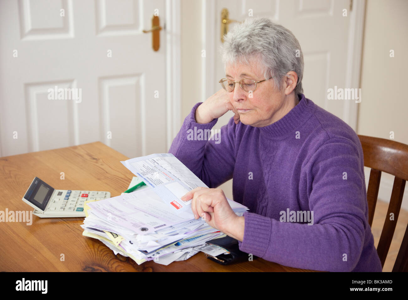 Anziana donna senior titolare di pensione o di rendita OAP lady pensionato con una grande pila di banconote sul tavolo cercando premuto ad un grande carburante gas bill. Regno Unito Gran Bretagna Foto Stock