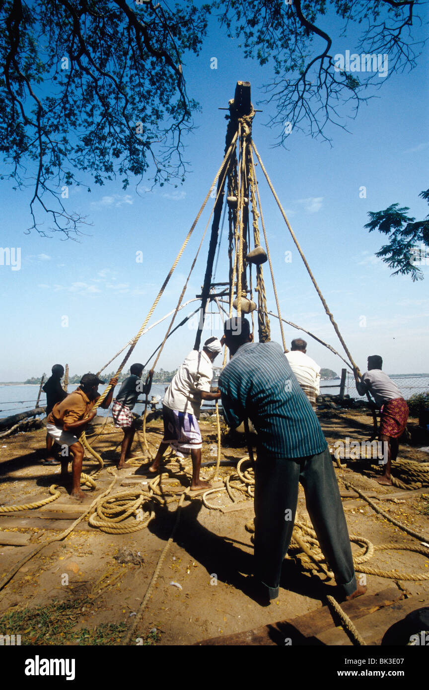 I pescatori operanti sui cinesi reti da pesca a Fort Cochin India Kerala Foto Stock