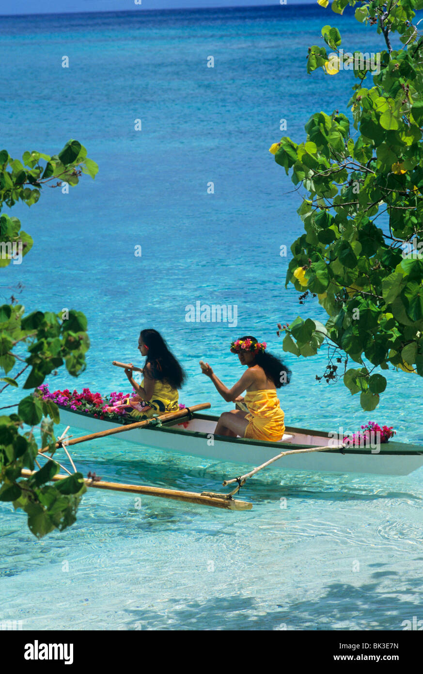 Due giovani donne racchetta una canoa outrigger attraverso una laguna sull isola di Huahine nelle isole della Società della Polinesia francese. Foto Stock