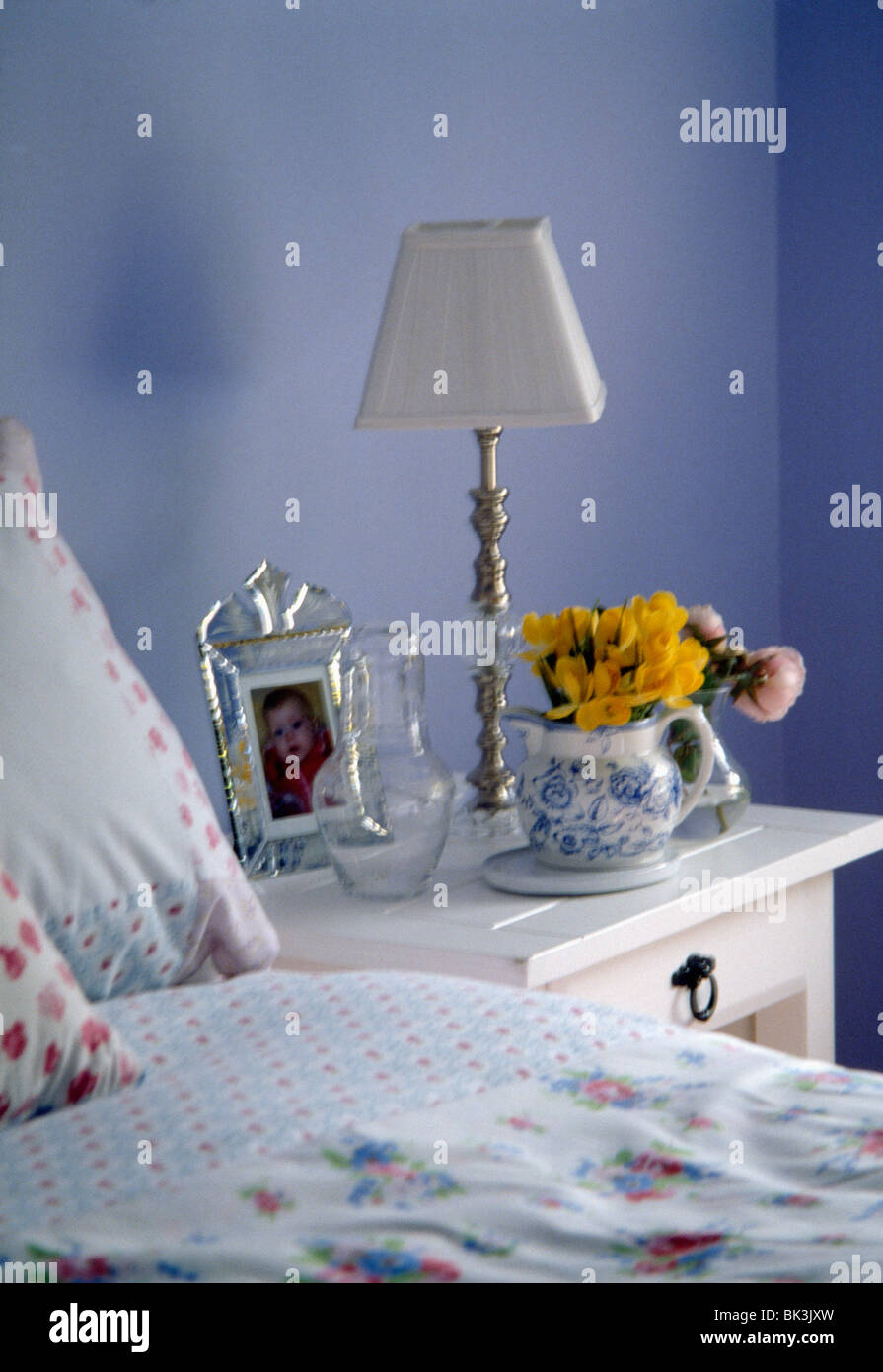 Lampada in metallo con paralume bianco sul comodino con brocca di fiori nel paese blu camera da letto Foto Stock