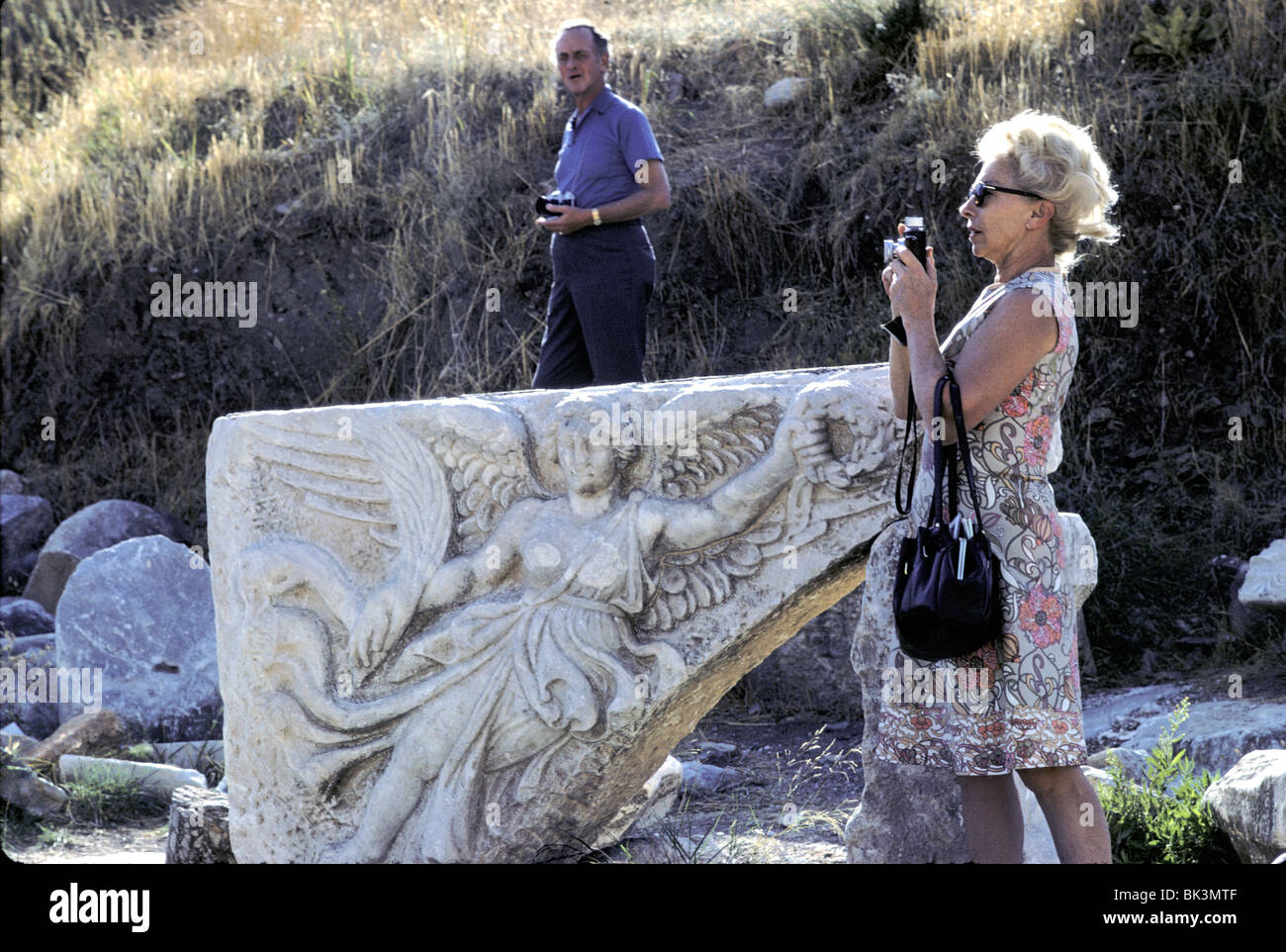 Turisti americani accanto a Marble bassorilievo di donna alata ghirlanda di contenimento e piuma. Efeso, Turchia, Ottobre 1971 Foto Stock