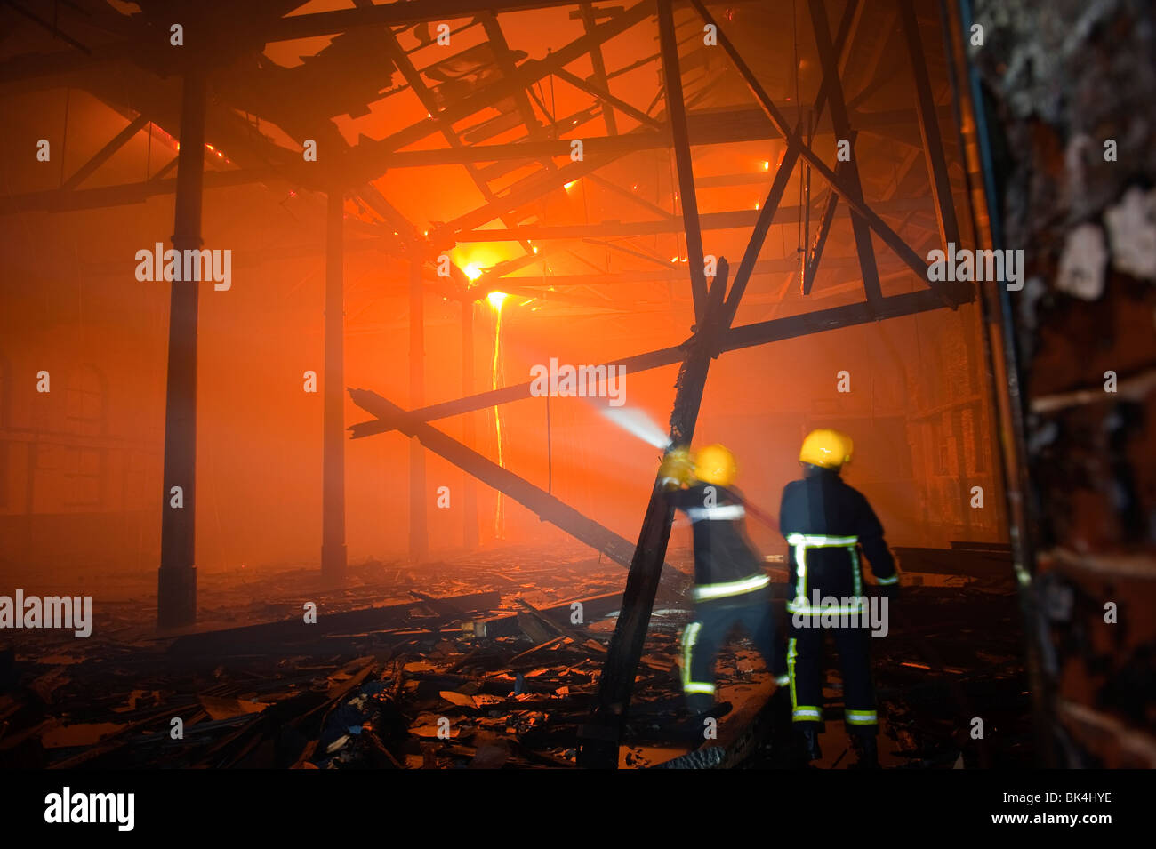 I vigili del fuoco all'interno del magazzino sul fuoco con travi del tetto sta crollando e fiamme Foto Stock