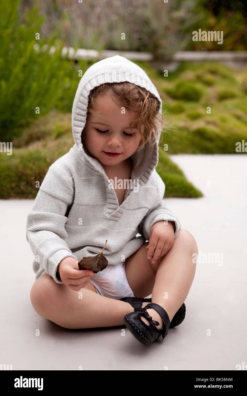 Il Toddler girl in felpa grigio seduto sul marciapiede Foto Stock