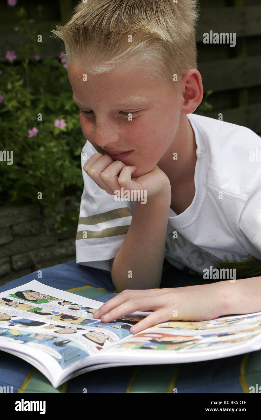 Ragazzo adolescente la lettura del libro di fumetti nel retro del giardino in estate vacanze al di fuori. Foto Stock
