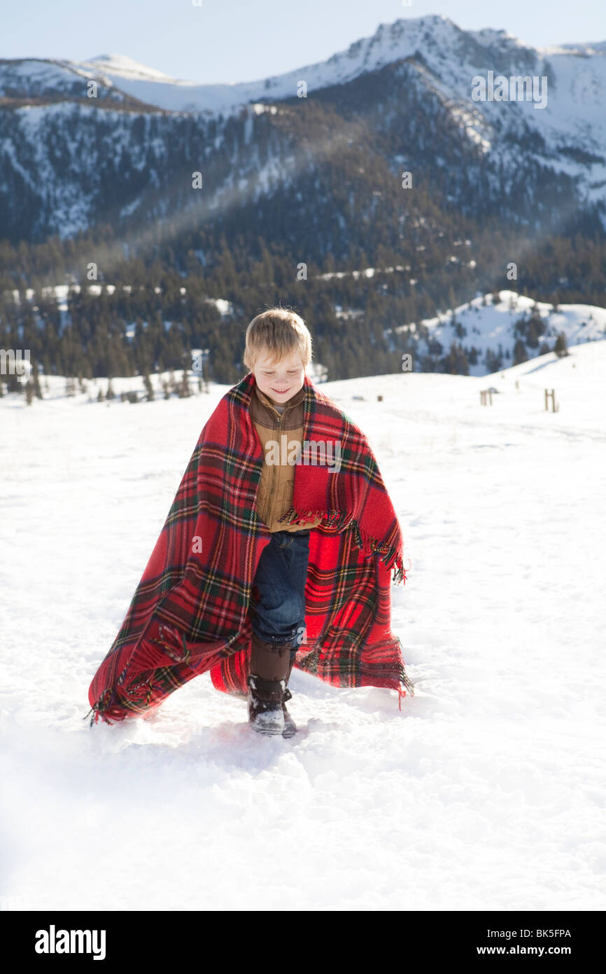 Ragazzo giovane avvolto in rosso plaid coperta a giocare nella neve Foto Stock