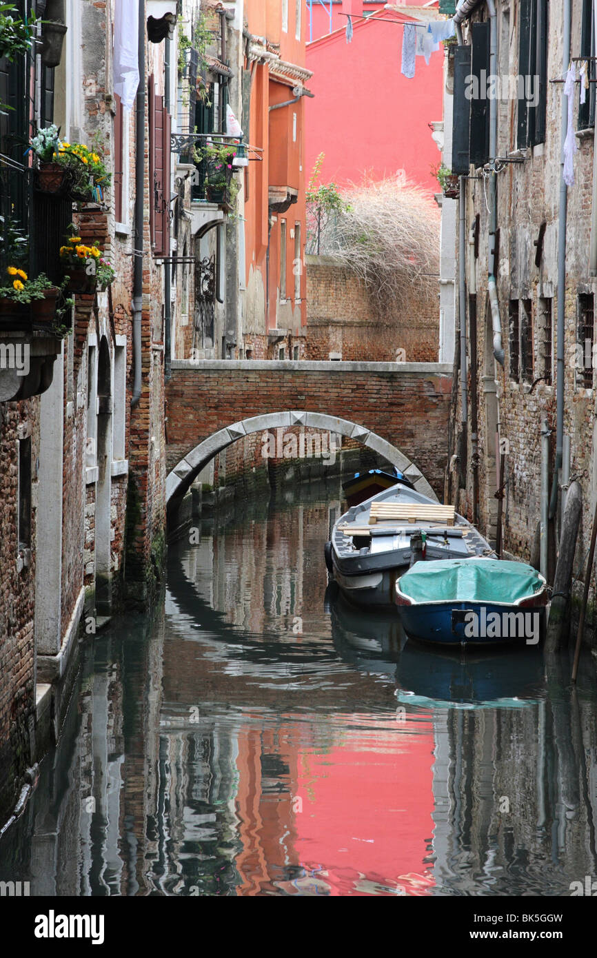 Canale veneziano con la costruzione di riflessioni, ormeggiate barche e tipico ponte veneziano. Foto Stock