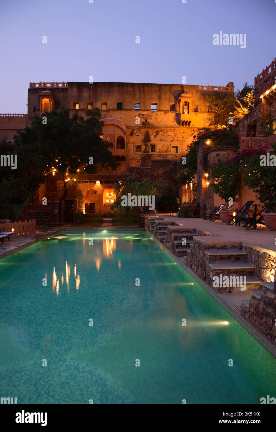 Di tronchi grezzi mura salgono su due lati del splendidamente illuminati piscina, Neemrana Fort Palace, Rajasthan, India Foto Stock