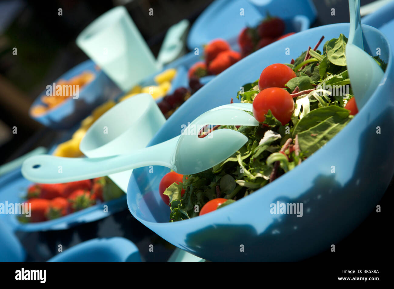 Pasto all'aperto o un picnic su una tavola nera con plastica blu bocce, coppe e brocche con frutta e insalata mista Foto Stock