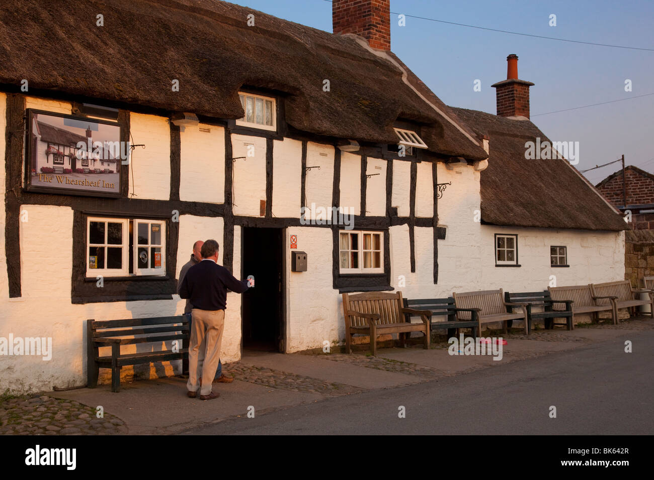 Un pub di campagna, England Regno Unito, Wirral, cottage con il tetto di paglia, con i bevitori si fermò fuori godendo la sera. Foto Stock