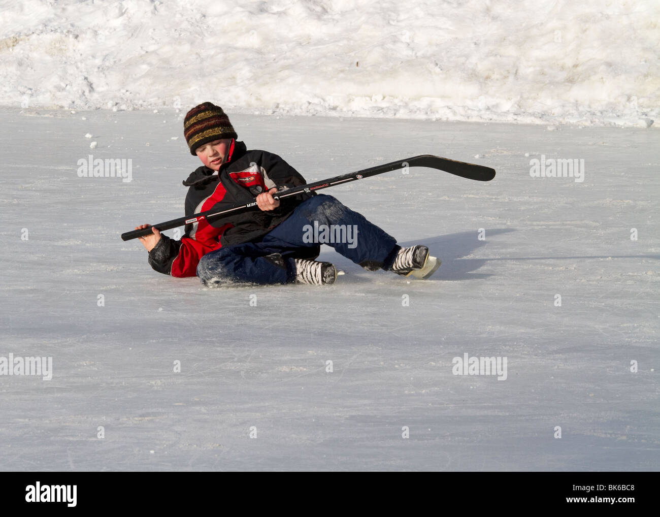 Ragazzo caduto sul ghiaccio con la mazza da hockey in inverno Foto Stock