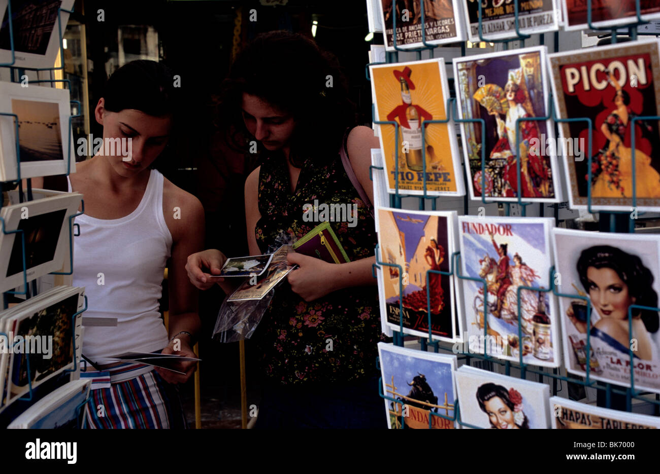 Due turisti femmina foglia attraverso vari cartoline al di fuori di un negozio nel centro di Siviglia, Spagna. Foto Stock