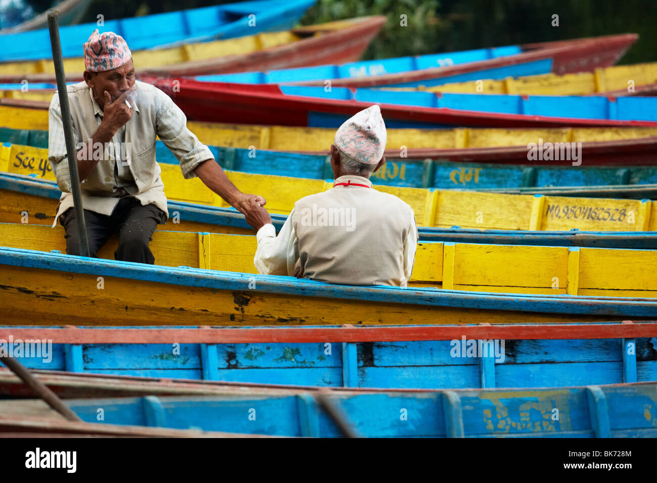 Due uomini anziani seduti su imbarcazioni a remi di condividere una sigaretta in Pokhara, Nepal. Foto Stock