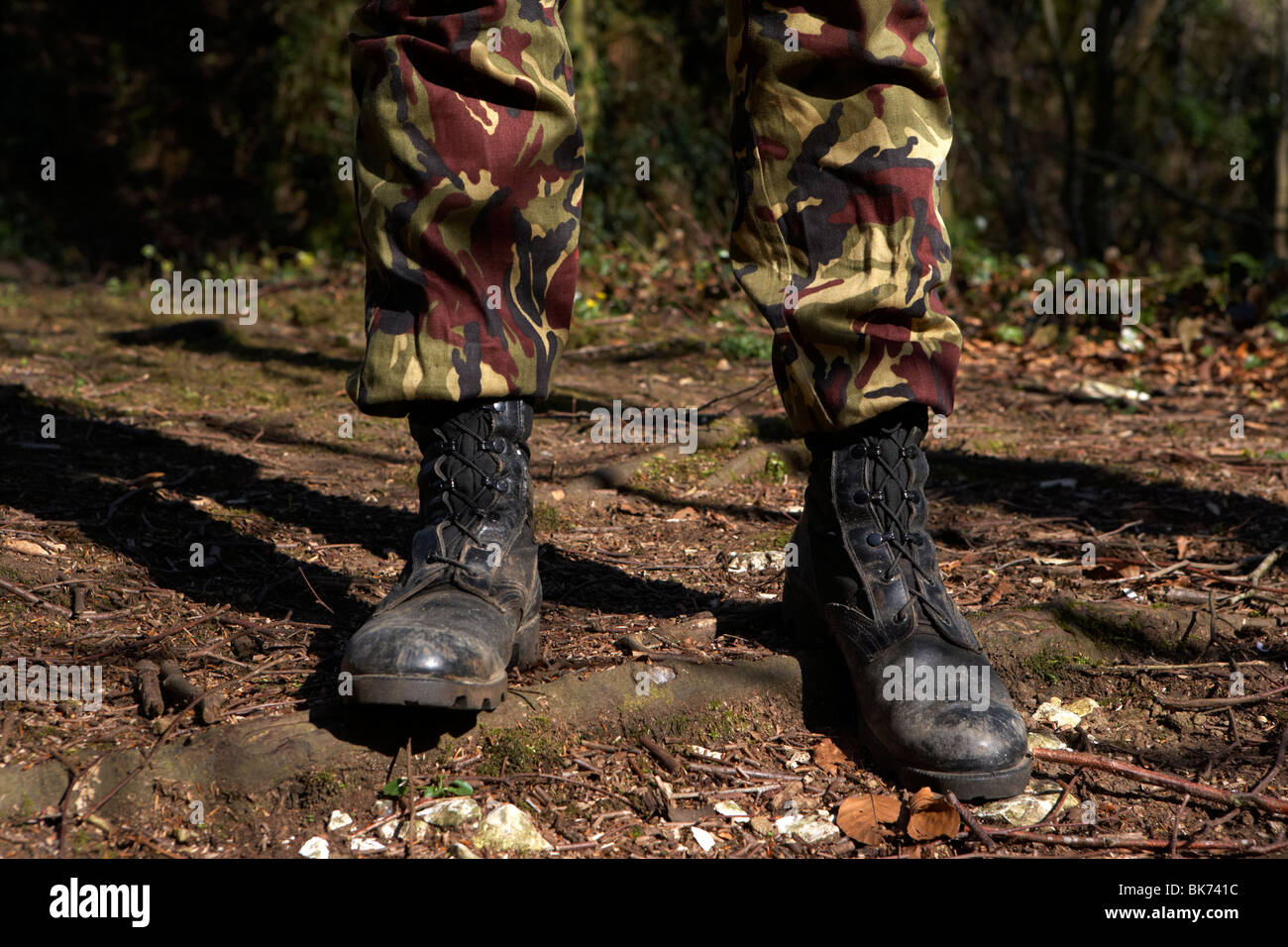 Uomo che indossa il camuffamento combattere i pantaloni e stivali in piedi a proprio agio in una foresta nel Regno Unito Foto Stock