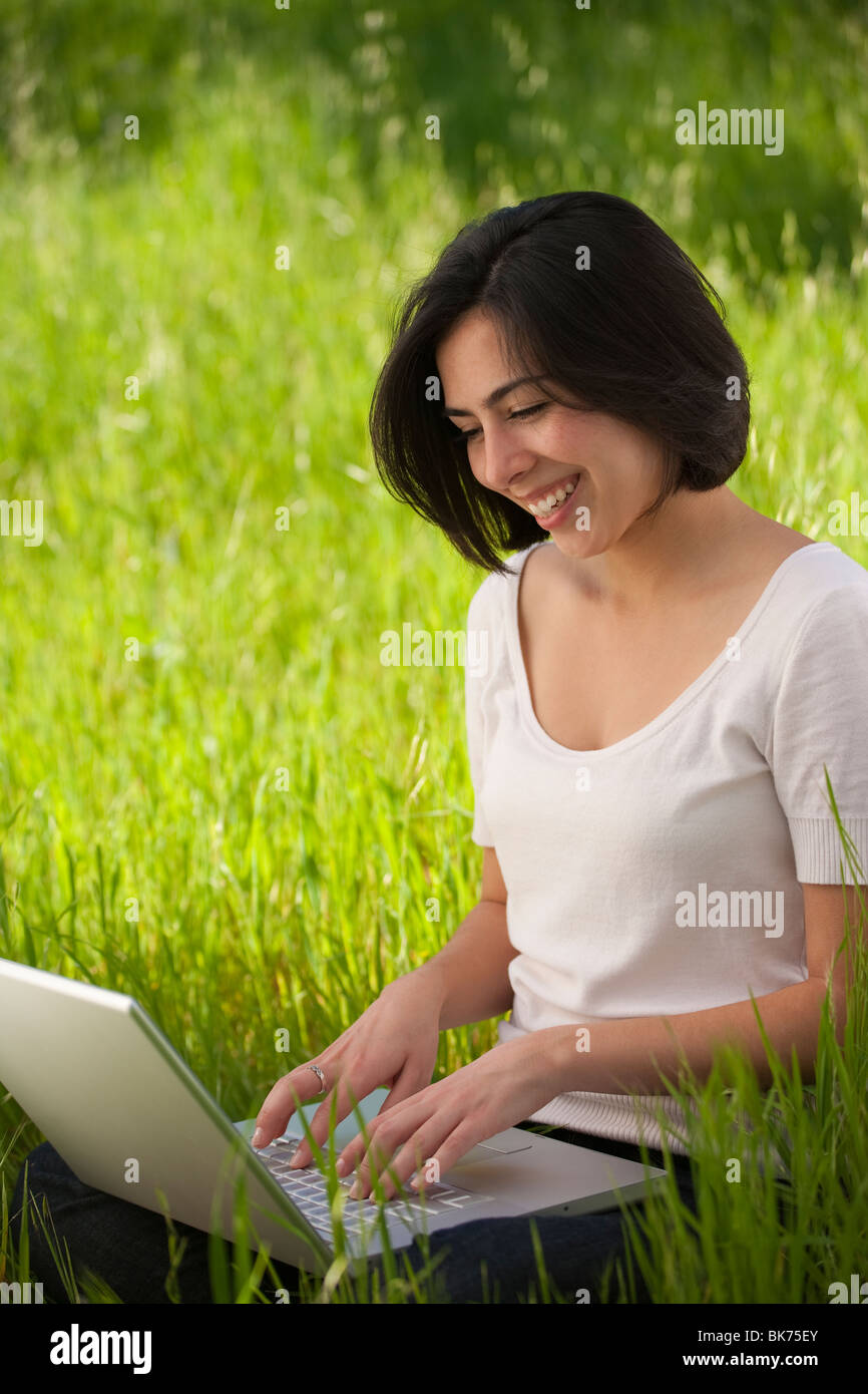 Bella, giovane donna ispanica lavorando su un computer portatile in un prato erboso Foto Stock