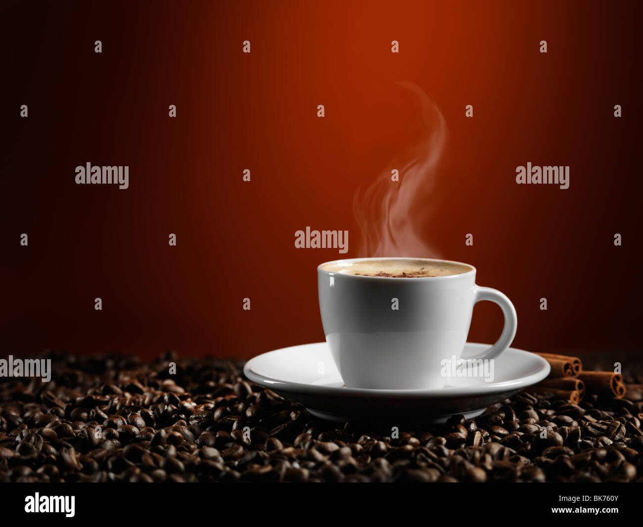 Tazza di caffè latte in piedi sul caffè in grani isolati scuro su sfondo rosso Foto Stock