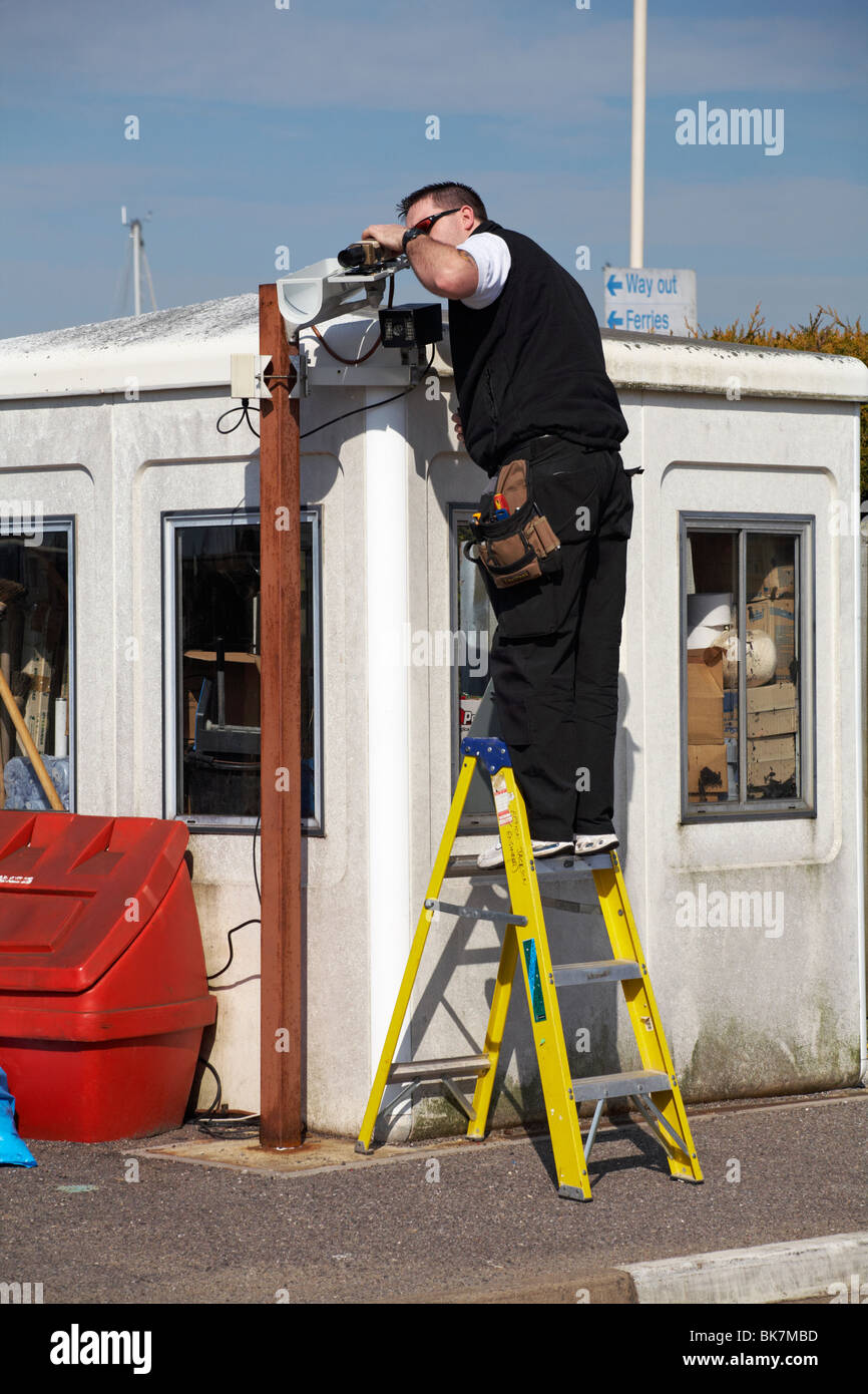 Ingegnere uomo in piedi su scala a gradini che lavora sul sistema CCTV al porto dei traghetti di Lymington, Lymington, Hampshire UK nel mese di aprile Foto Stock
