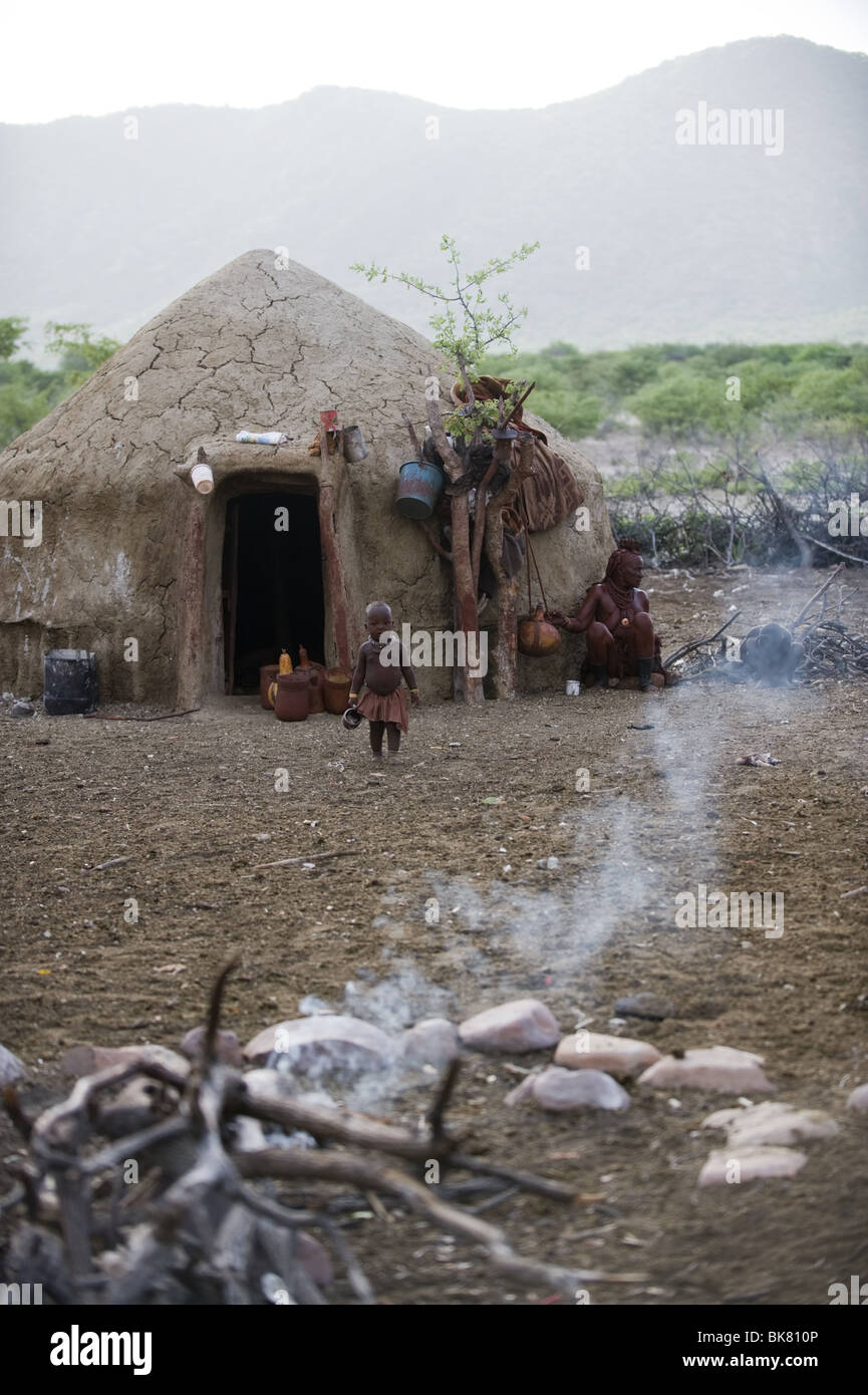 Donna Himba capanna esterna con un bambino a camminare verso il fuoco santo Kaokoland, Namibia. Foto Stock