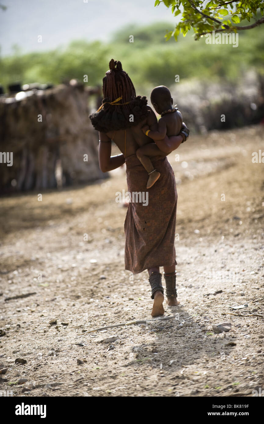 Himba donna di trasportare un bambino, Kaokoland, Namibia Foto Stock