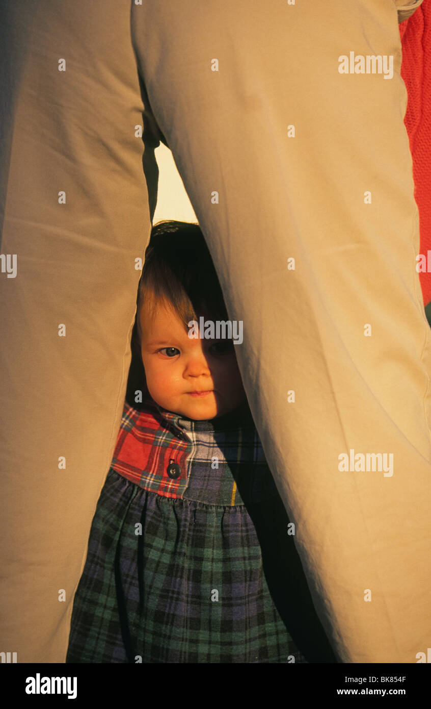 Un bambino di 18 mesi ragazza picchi toddler tra la sua mamma per le gambe Foto Stock