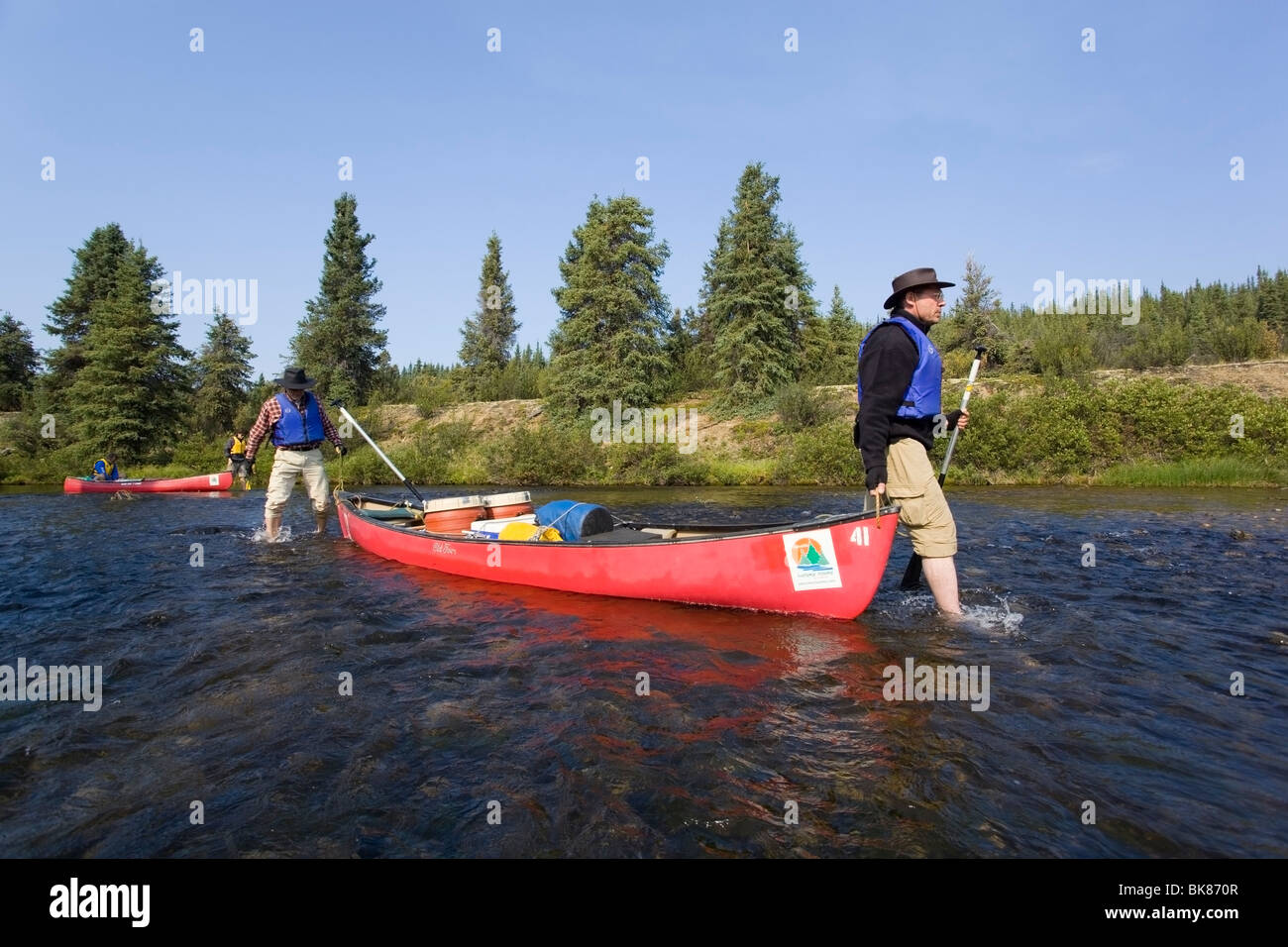 Due uomini fodera canoa, camminare a piedi nudi Nello shallow Caribou Creek, superiore Liard River, Yukon Territory, Canada Foto Stock