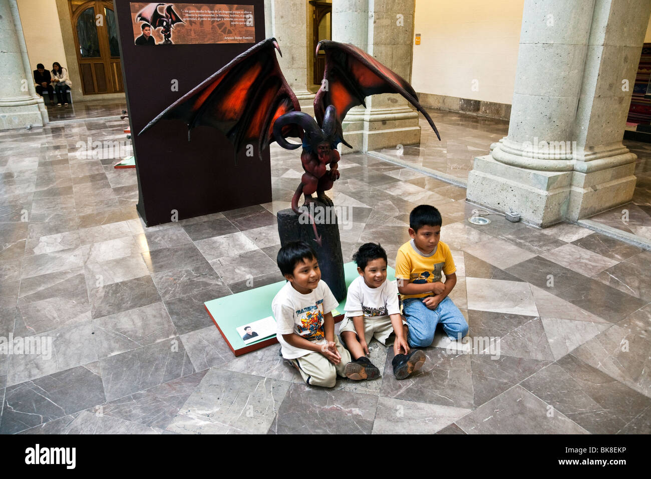 Tre piccoli boyschildren messicano pongono di fronte scary meditabondo dragon scultura in mostra a Oaxaca governatori Palace Mexico Foto Stock