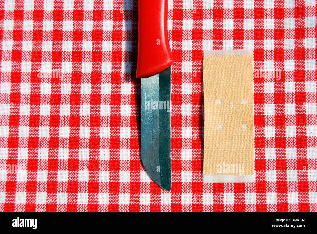 Coltello rosso e banda-aiuto sulla tovaglia scozzese Foto Stock