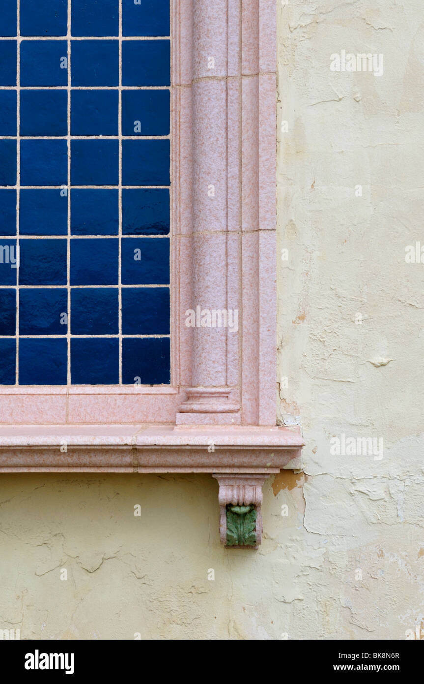 Un colorato con piastrelle blu finestra con telaio rosa in una parete in stucco. Old.Closeup Foto Stock