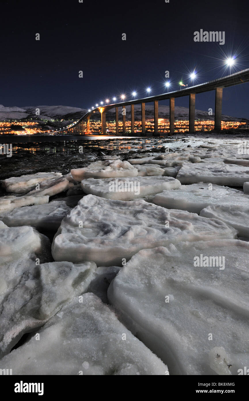 Ponte su una notte invernale con lampioni. Ice floes in primo piano. Il ponte di collegamento Sandnessundbrua Tromso e Kvaloya Foto Stock