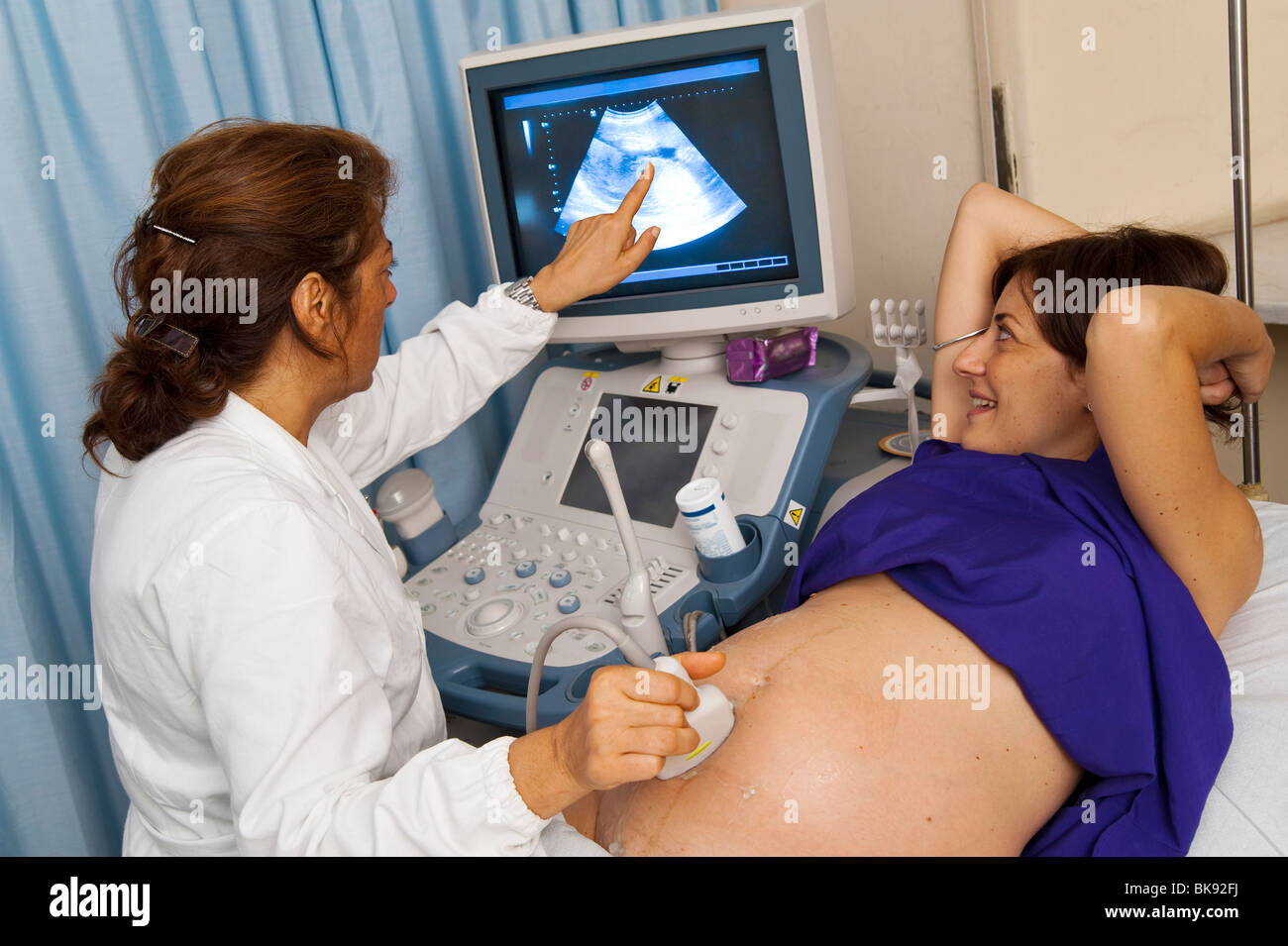 Medico rivolto a schermo durante la scansione a ultrasuoni dello stomaco di una donna in stato di gravidanza Foto Stock