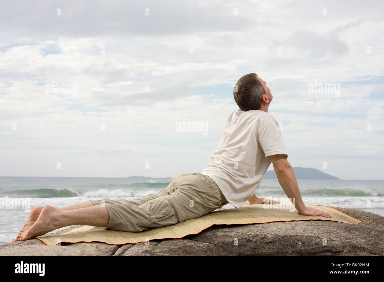 Uomo maturo facendo esercizi yoga su una roccia sul mare Foto Stock