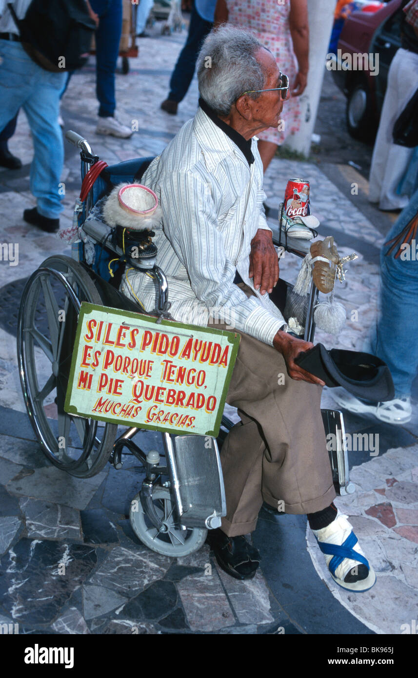 Un uomo con un piede bendato in una sedia a rotelle decorate con scarpe, elemosinare (con un segno in spagnolo). Veracruz, Messico Foto Stock