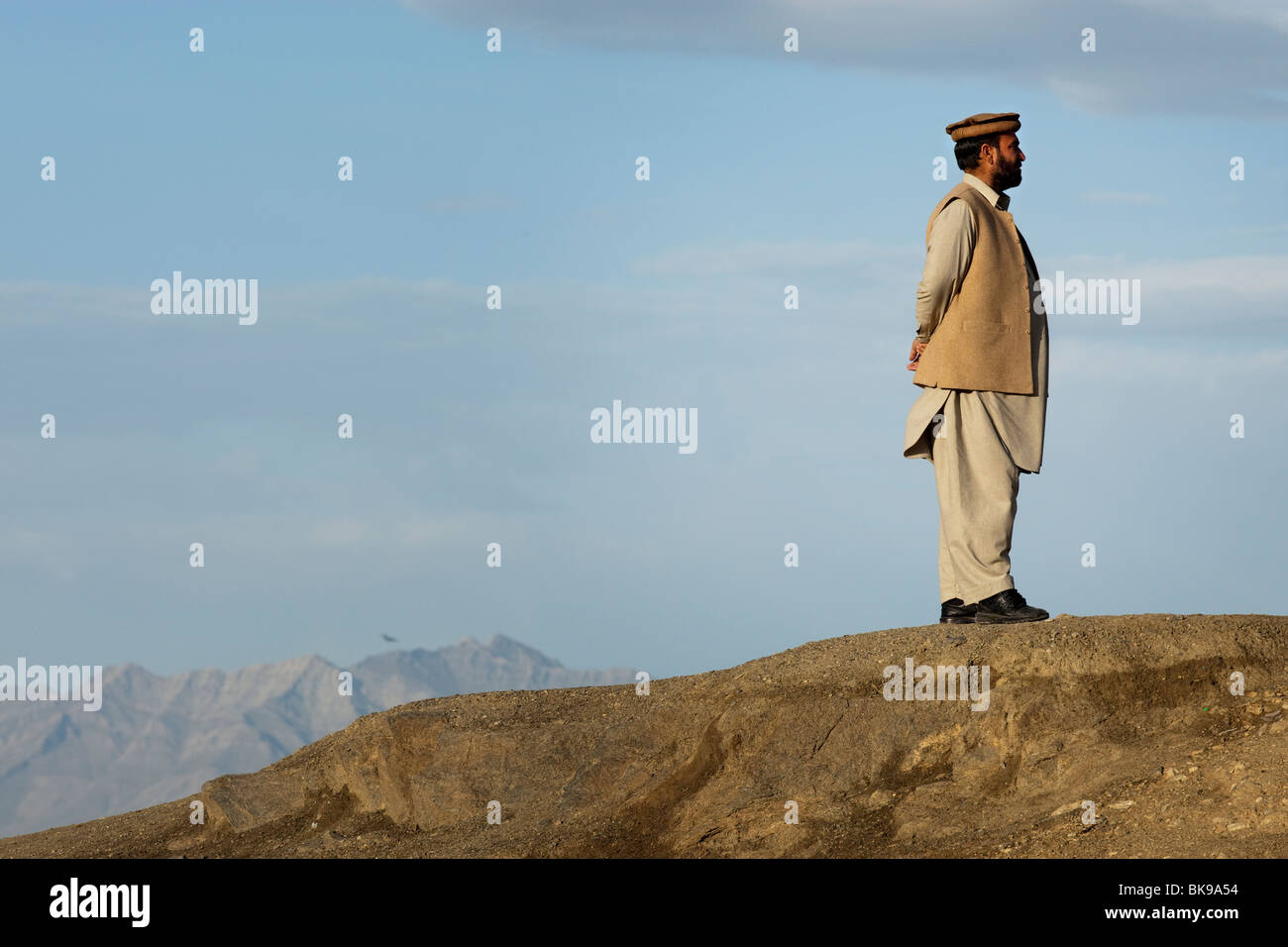 Un uomo afghano sorge su una collina che si affaccia su Kabul vestito in abiti tradizionali Foto Stock
