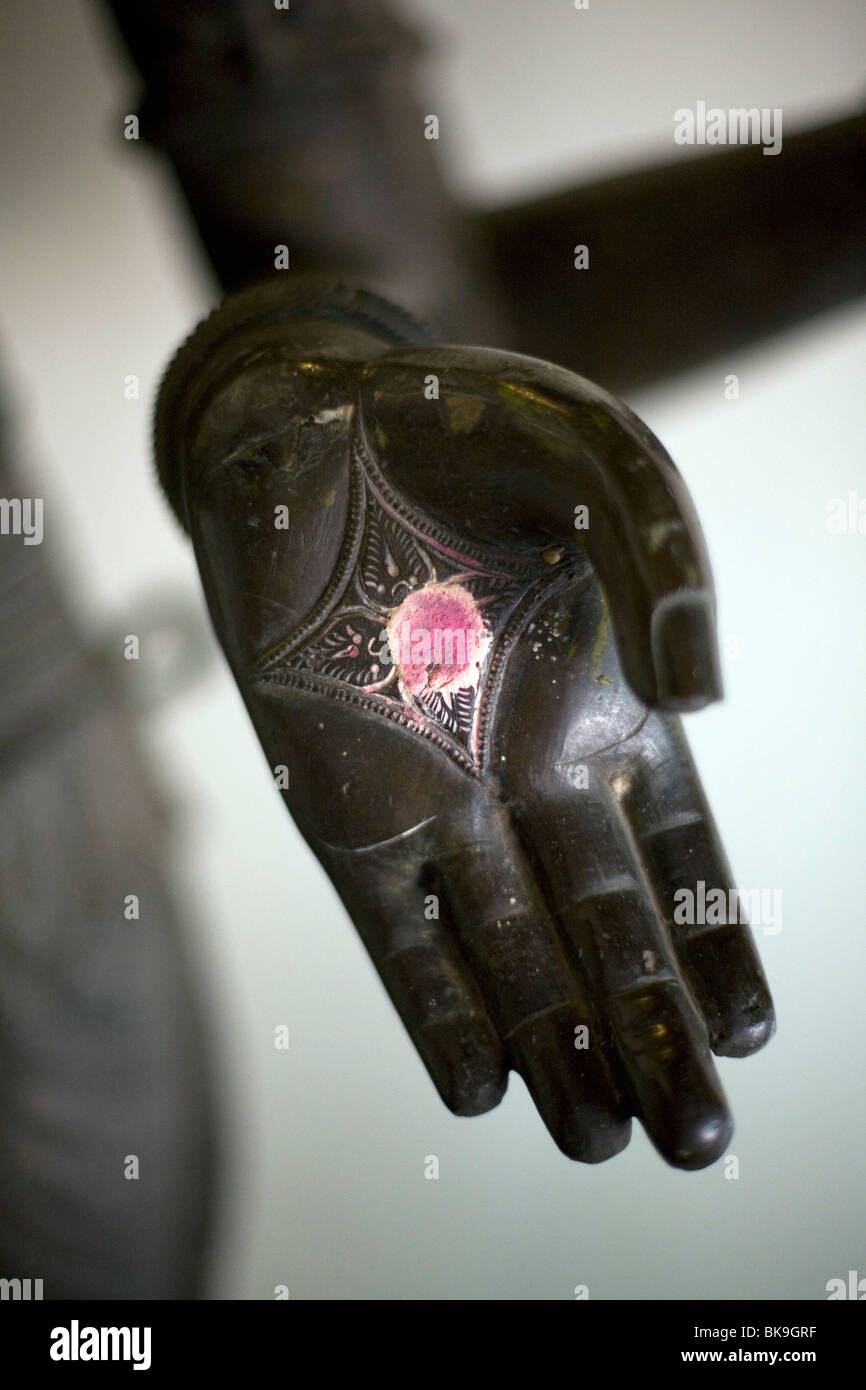 La mano di una statua di bronzo di una divinità Indù tenendo un vermiglio cospargere (vumvum) come un segno di benedizione (puja). Foto Stock