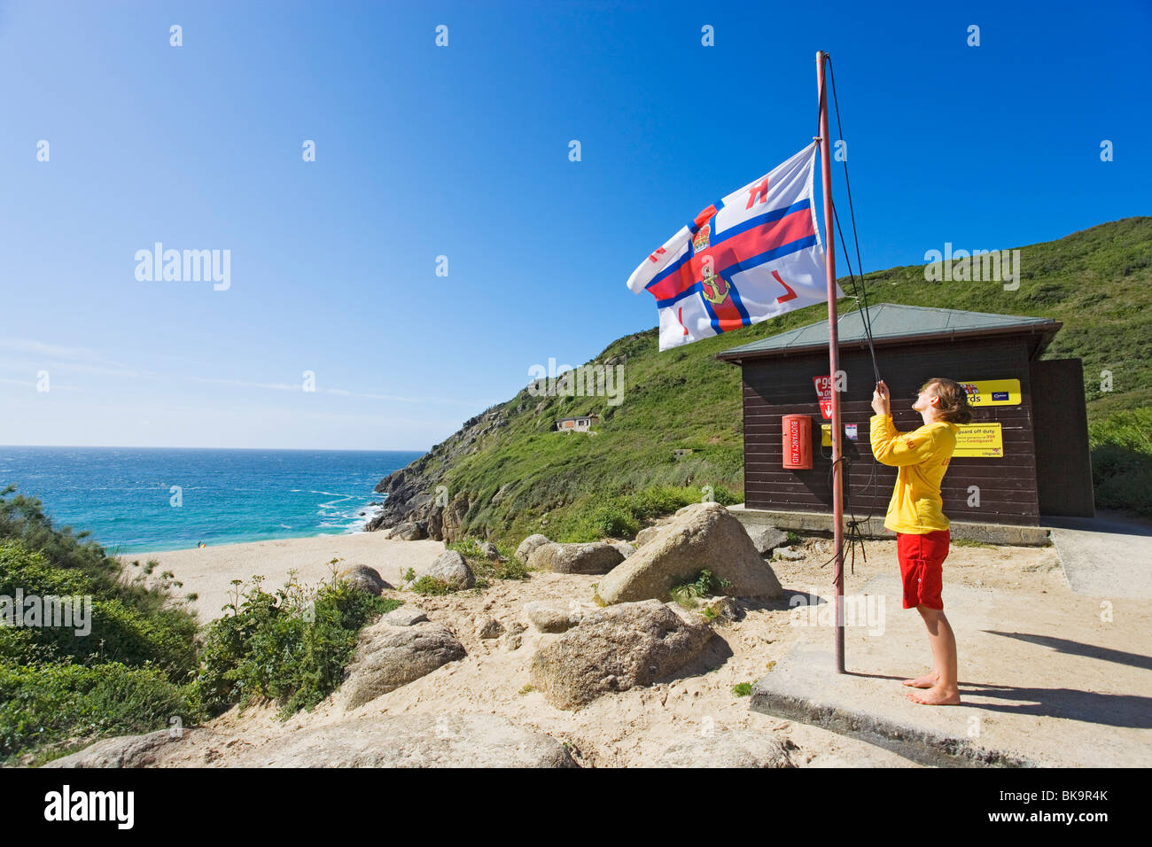 Donna battenti una bandiera, Porthcurno Beach, penisola di Penwith, Cornwall, England, Regno Unito Foto Stock