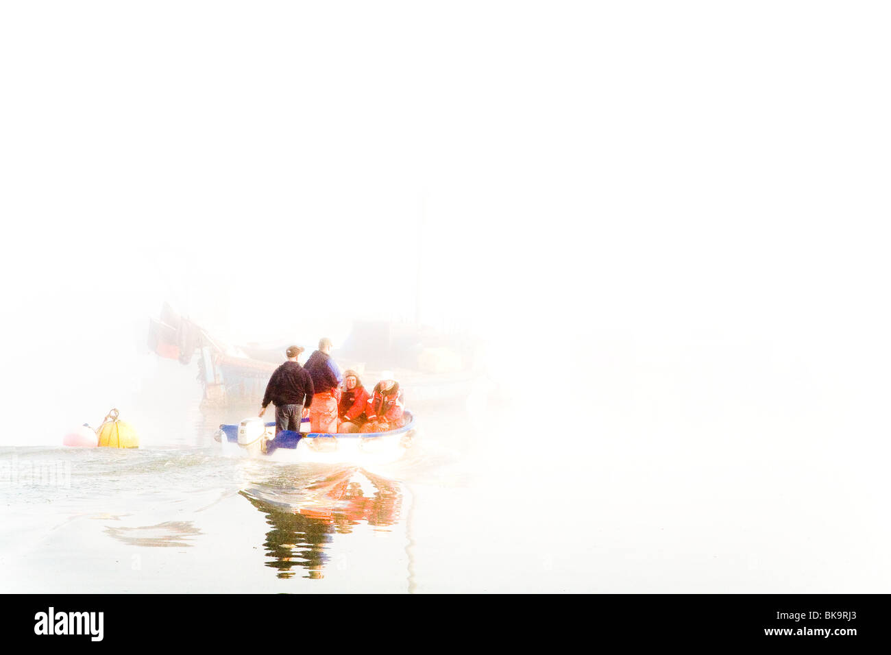 Una piccola barca con pescatori, teste fuori per la loro barca più grande nelle prime ore del mattino la nebbia Foto Stock